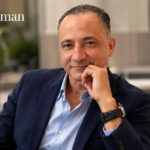 Carlos Alman sitting in a smart casual outfit against an elegant blurred background