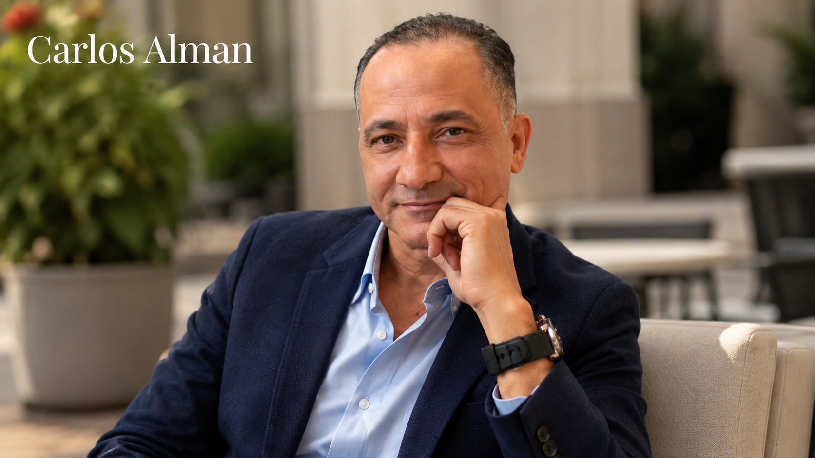 Carlos Alman sitting in a smart casual outfit against an elegant blurred background